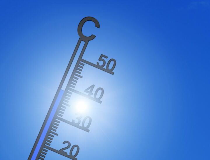 Thermometer showing high temperature with a clear blue sky and bright sun in the background