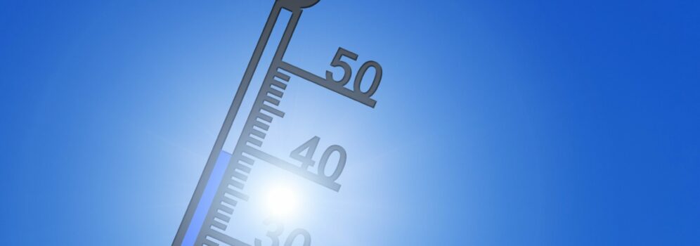 Thermometer showing high temperature with a clear blue sky and bright sun in the background